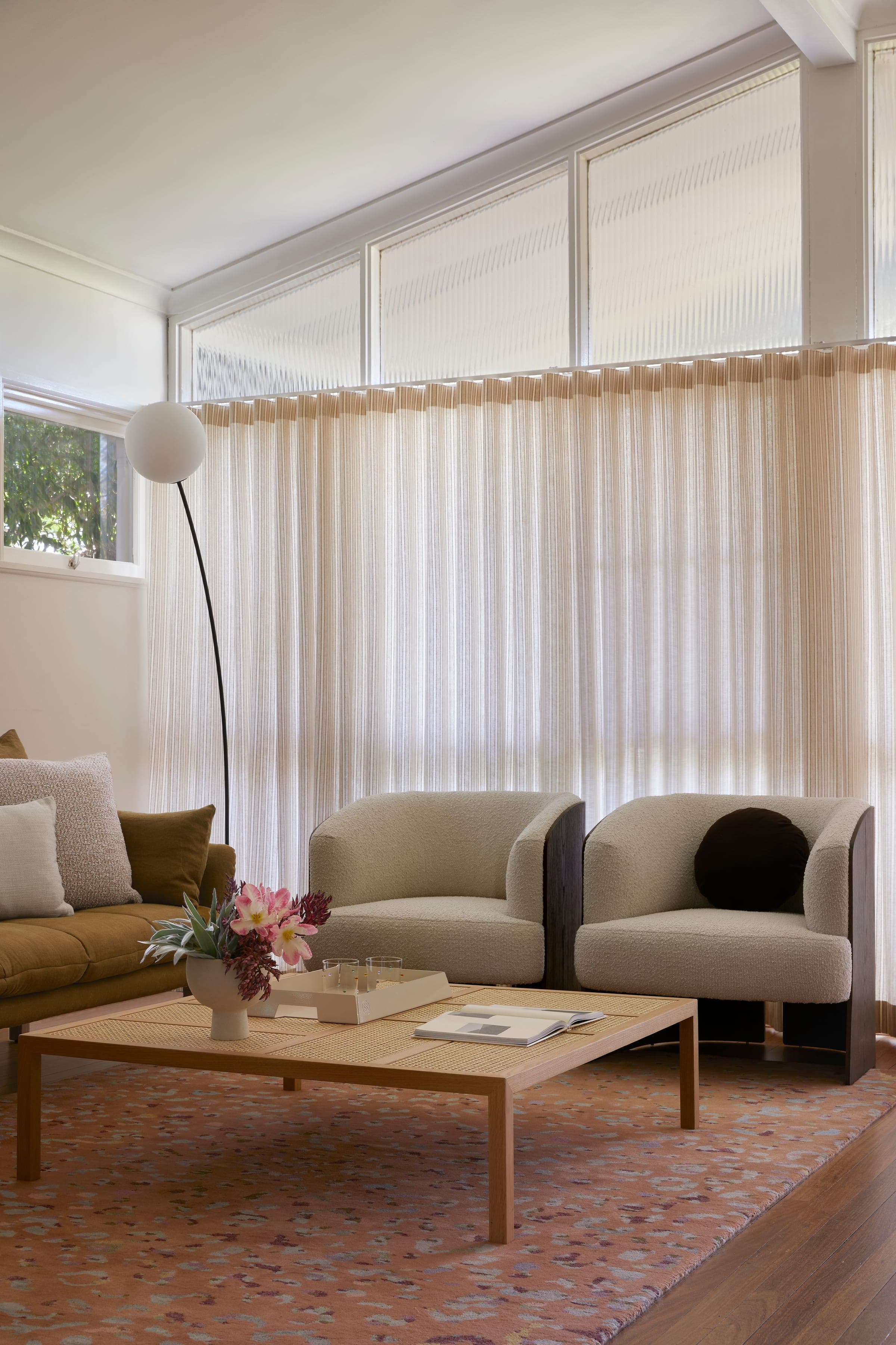 Living room showing the original fluted glass clerestory above a floor-length striped curtain, with olive sofa and boucle armchairs.