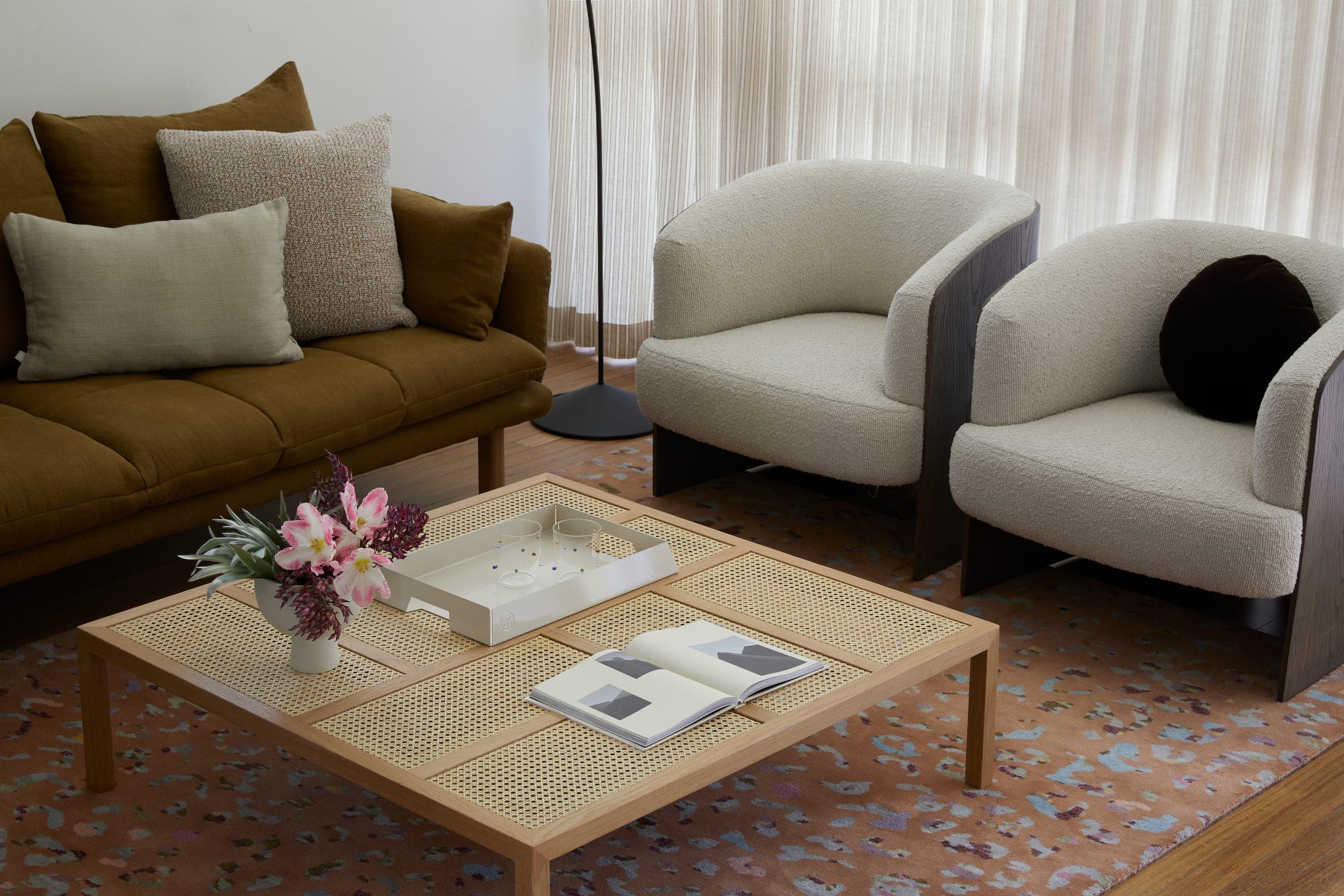 Cane coffee table with a ceramic tray and dried flowers in front of the olive sofa and boucle armchairs.