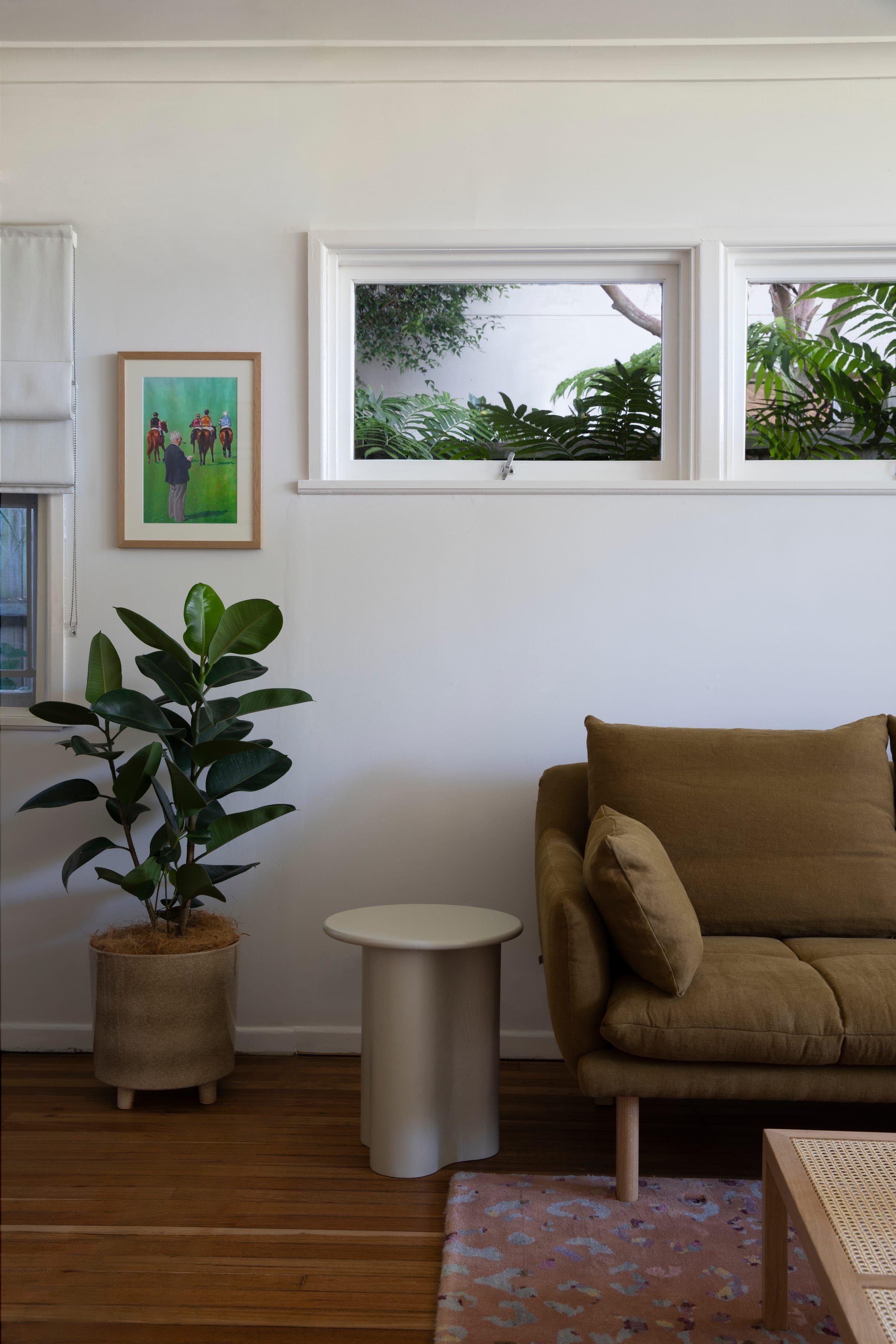 Reading nook with an olive linen armchair, sculptural side table, rubber plant and a clerestory window framing the garden.