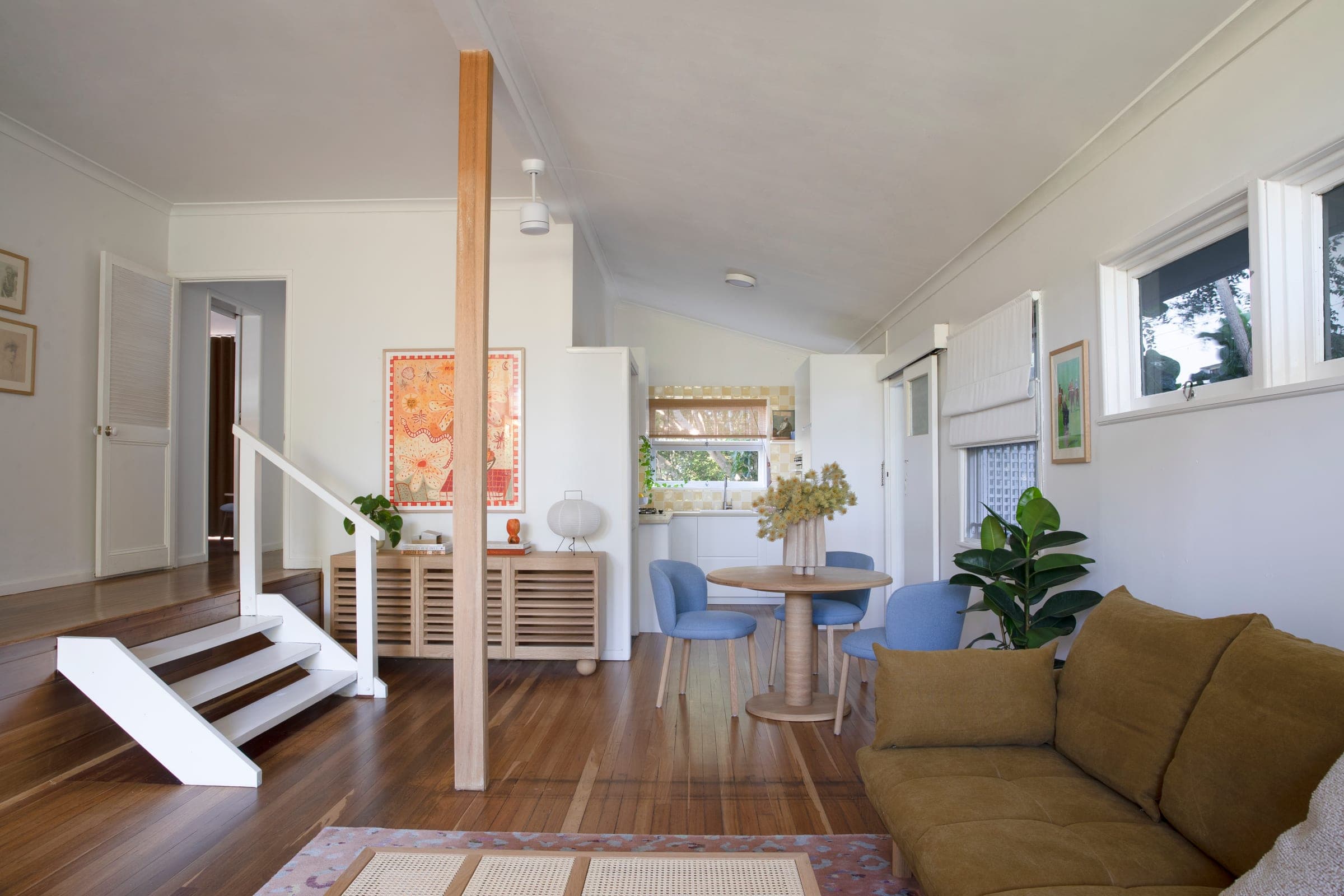 Open-plan living, dining and kitchen sequence with vaulted ceiling, original timber floors and a centred timber post.