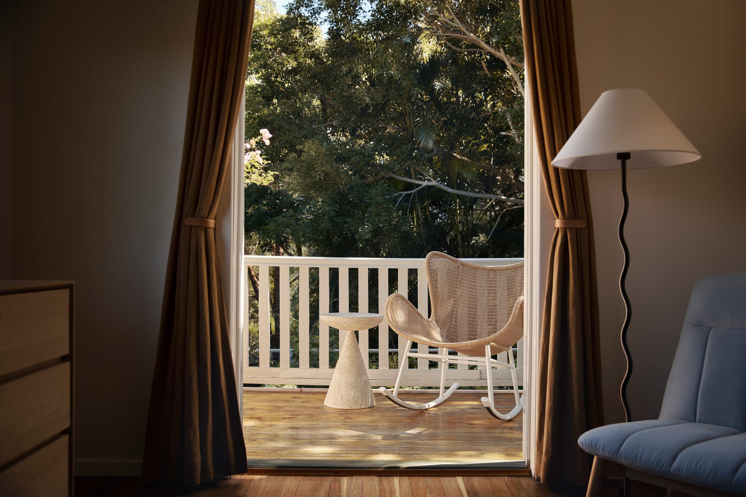 View from the bedroom through gold curtains to the balcony rocking chair and garden beyond.