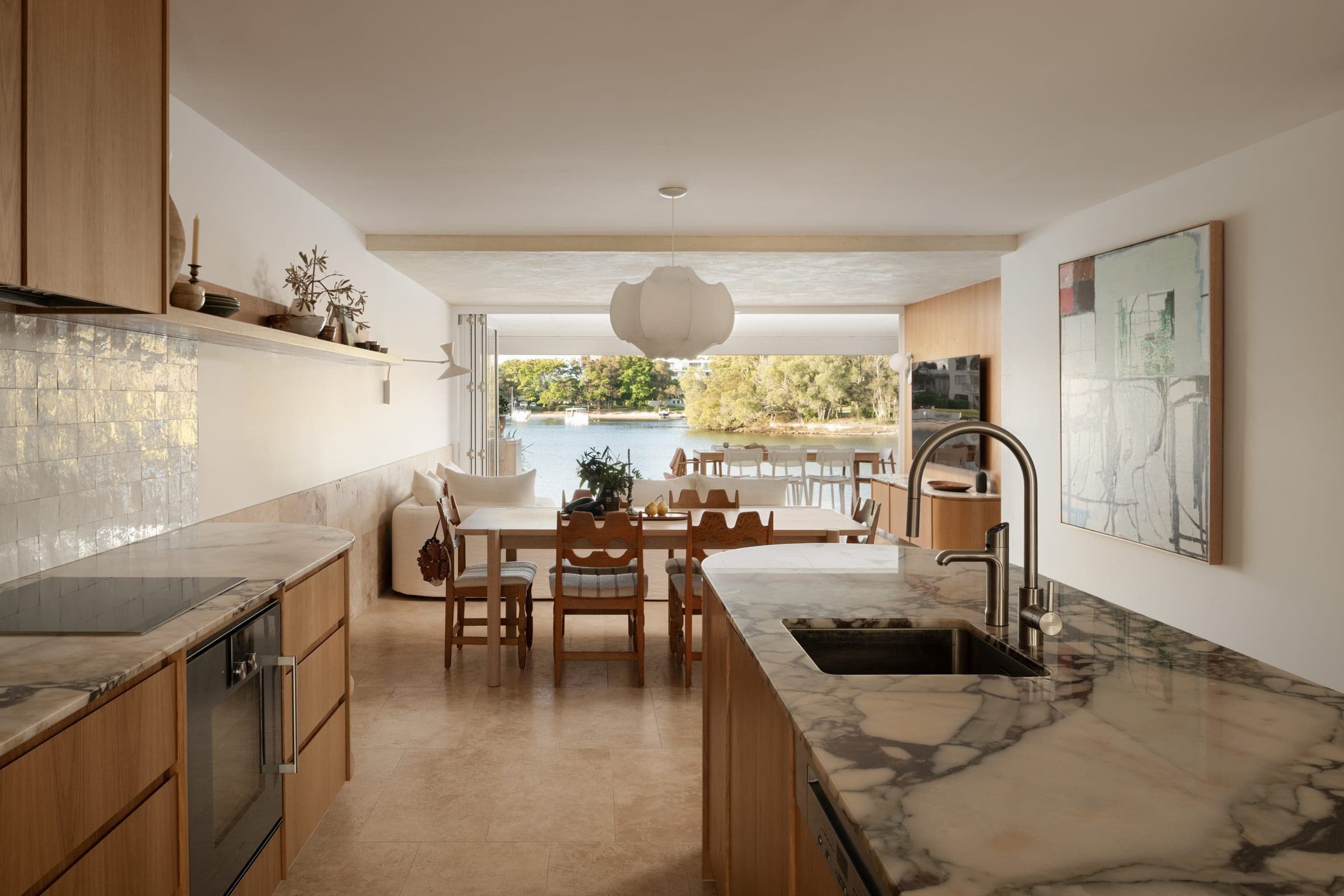 Open kitchen, dining and living sequence with bifolds pushed back to the river view, marble island in the foreground.