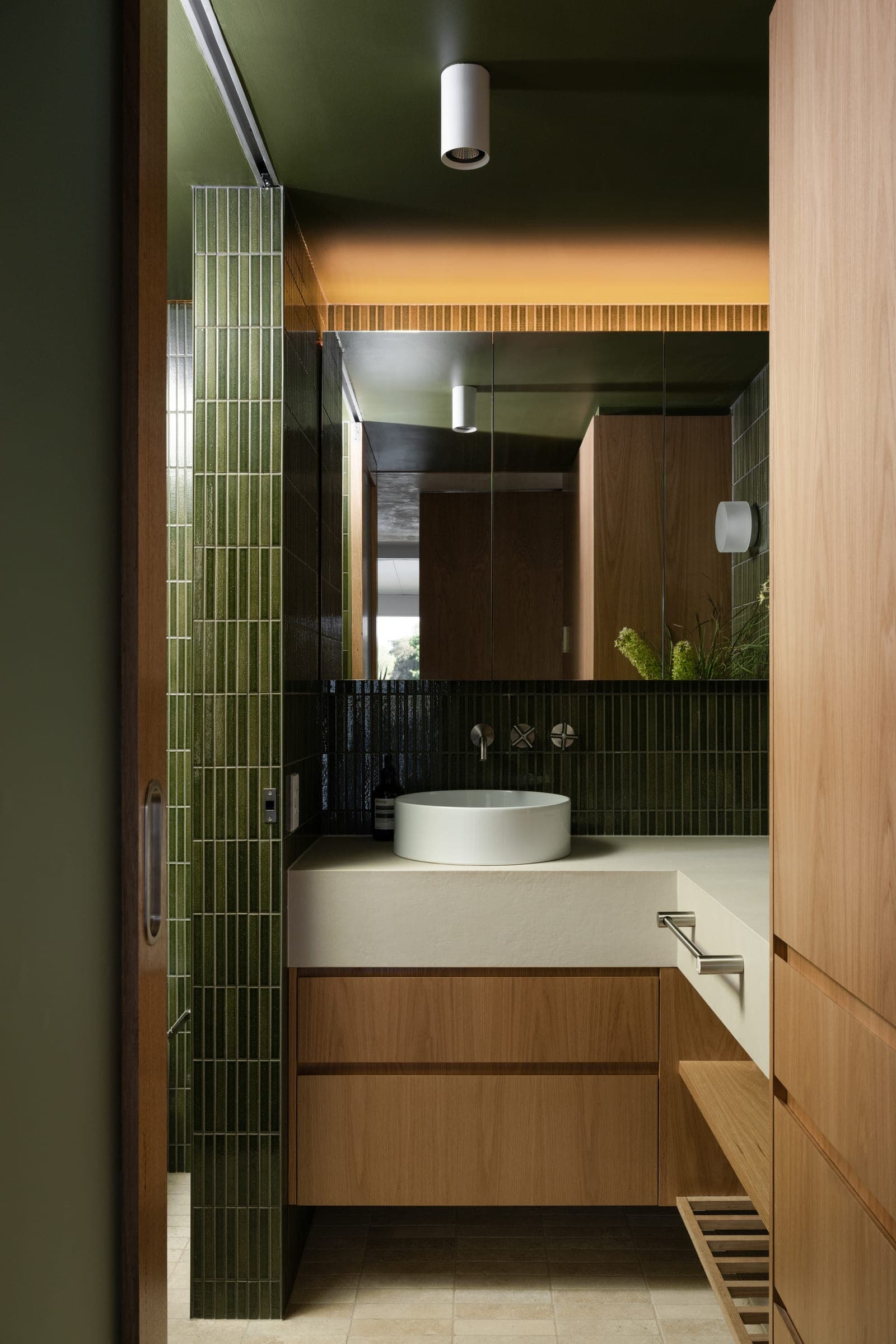 Powder room with vertical olive zellige, a stone vessel basin on a stone bench, oak vanity below and a fluted timber screen above the mirror.
