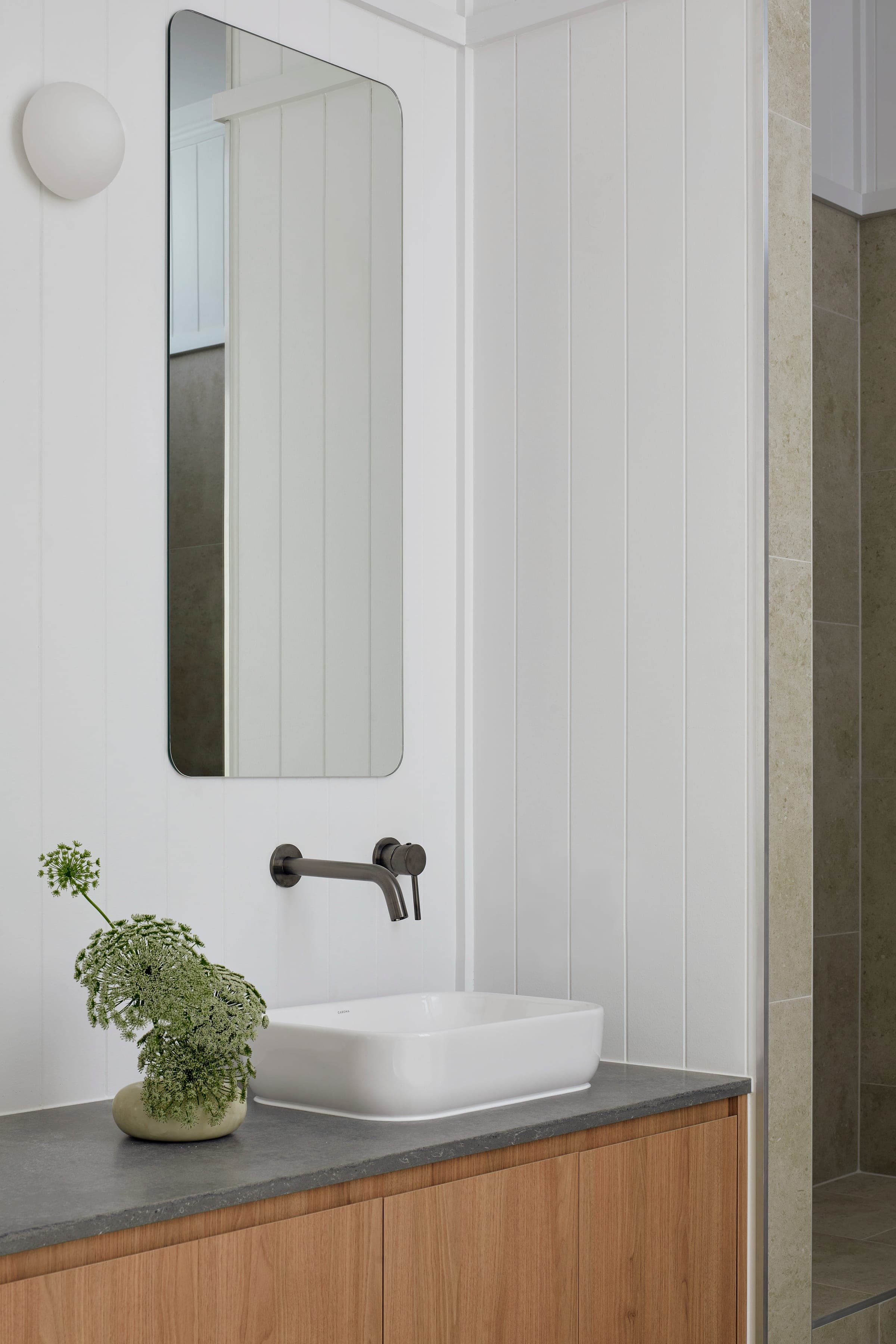 Powder room with white shiplap walls, oak vanity with grey stone top, vessel basin and Queen Anne's lace in a small vase.