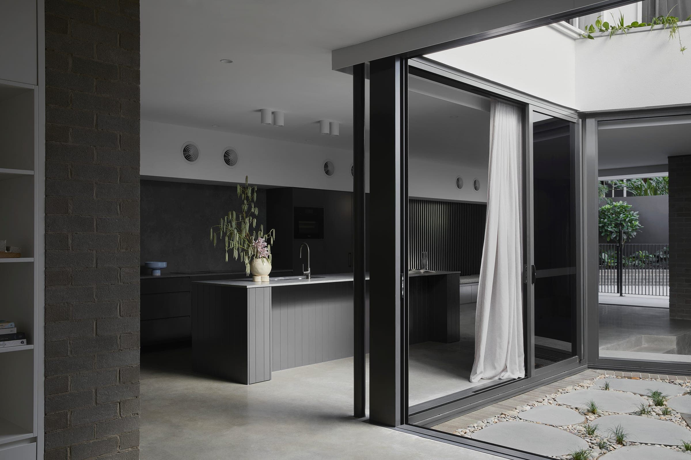 Black kitchen island and dark joinery alongside the sliding doors that open to the courtyard.