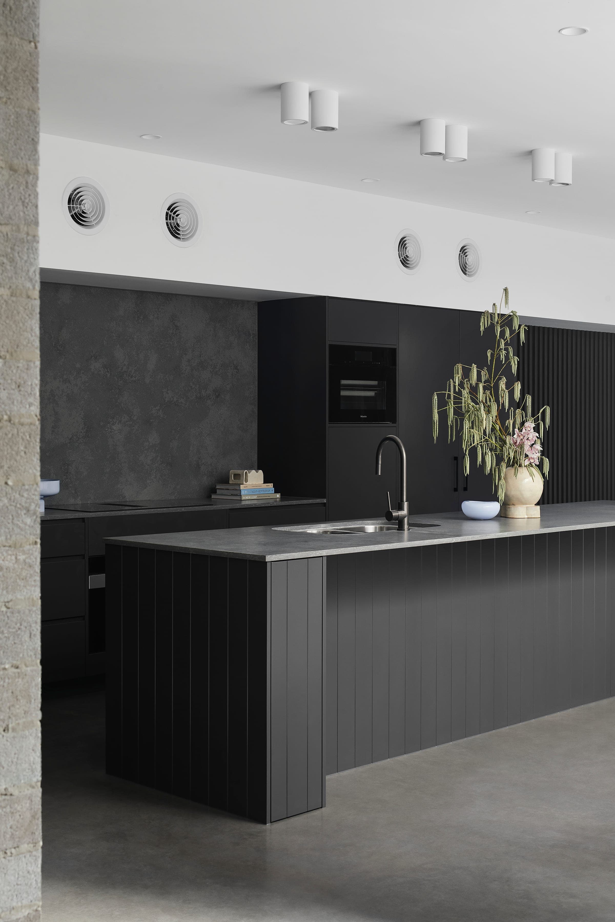 Detail of the black vertical-shiplap kitchen island with grey stone benchtop, sculptural ceramic vase and black tapware.