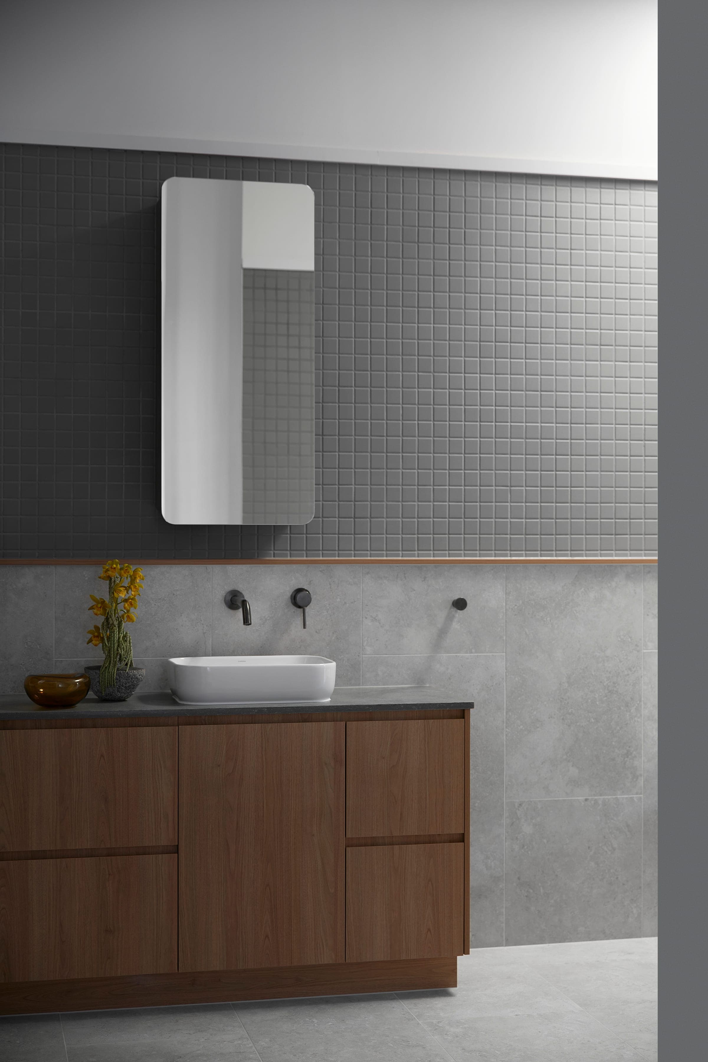 Bathroom with grey mosaic-tile wall, walnut vanity, vessel basin, black tapware and yellow daffodils on the bench.