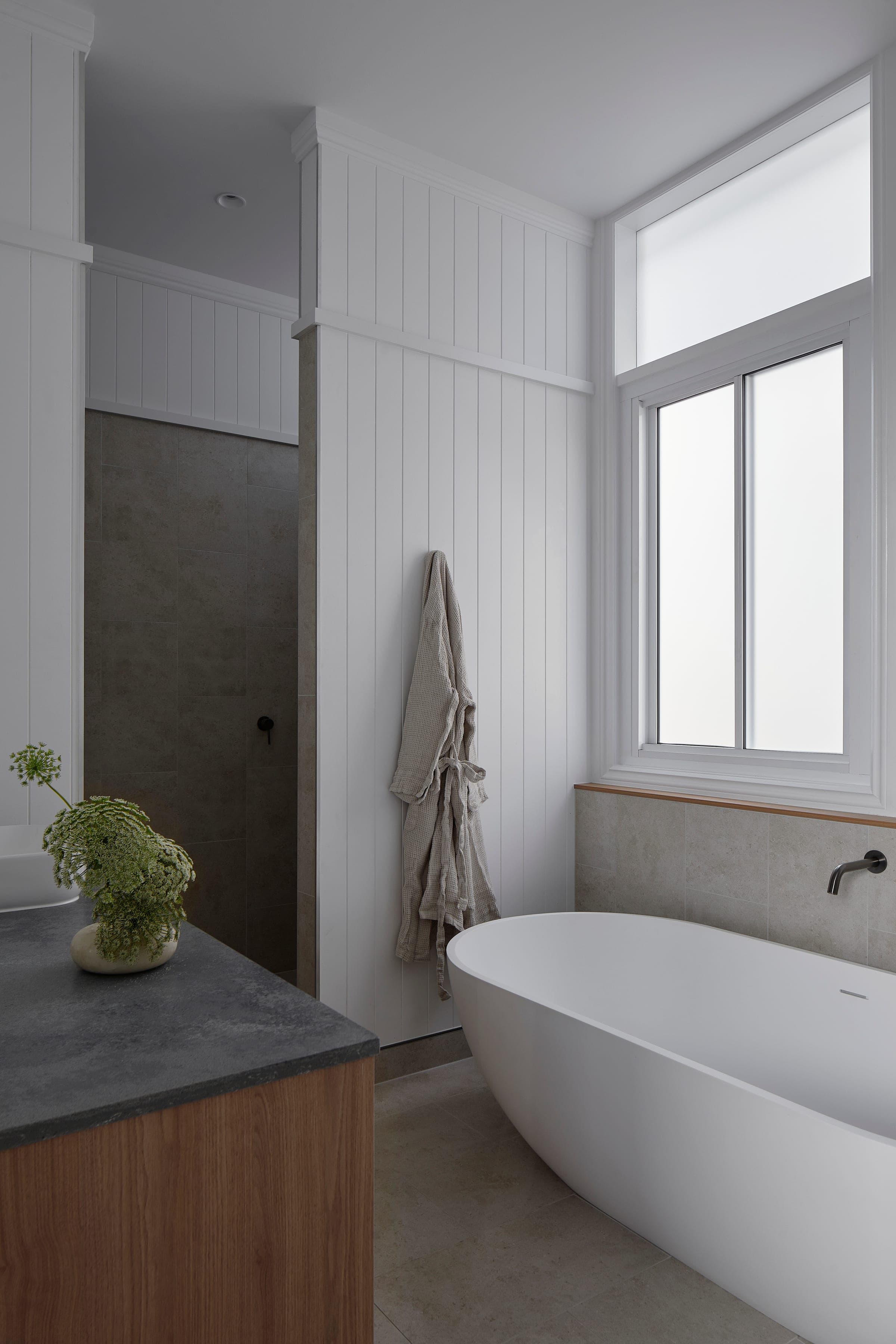 Light-filled bathroom with shiplap walls, freestanding tub under a window and a walnut vanity with stone top.