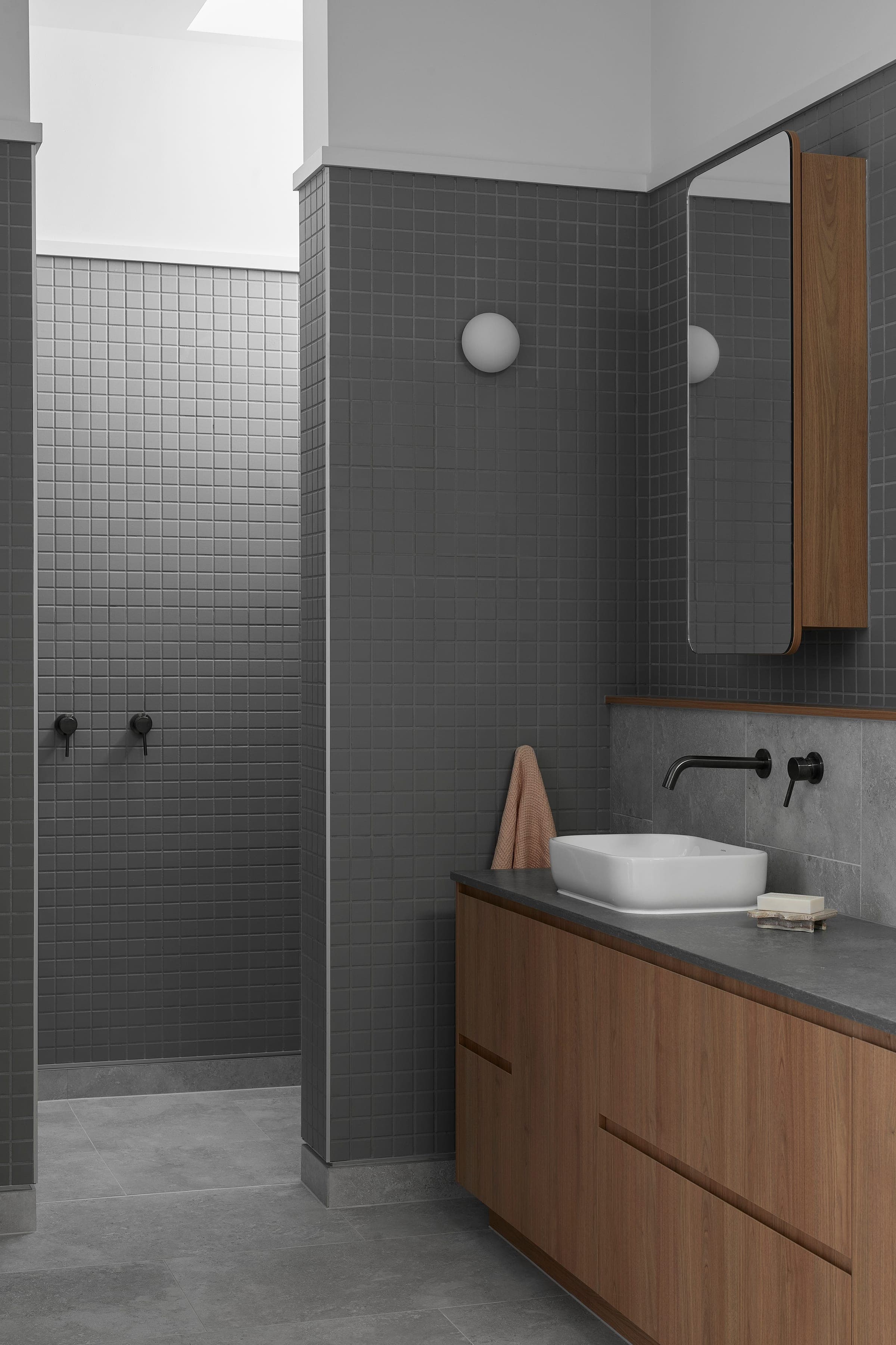 Full-height grey mosaic tile wraps the wet zone, with a walnut floating vanity and rectangular mirror cabinet.
