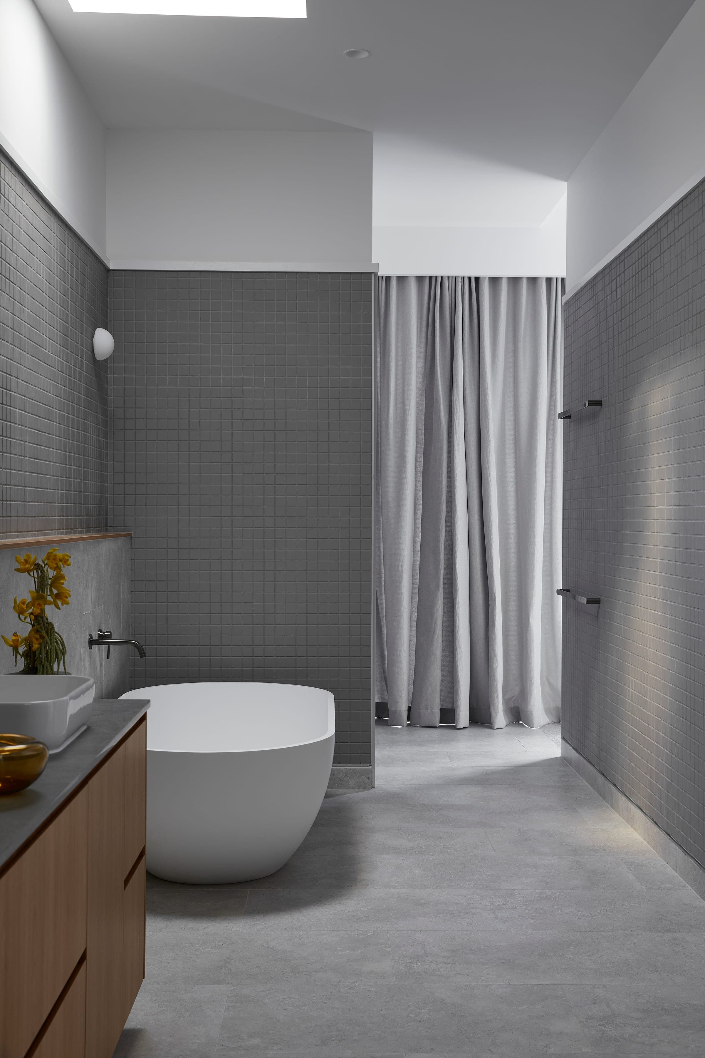 Bath area with grey mosaic walls, a sculptural freestanding tub and a full-height sheer curtain dividing the shower.